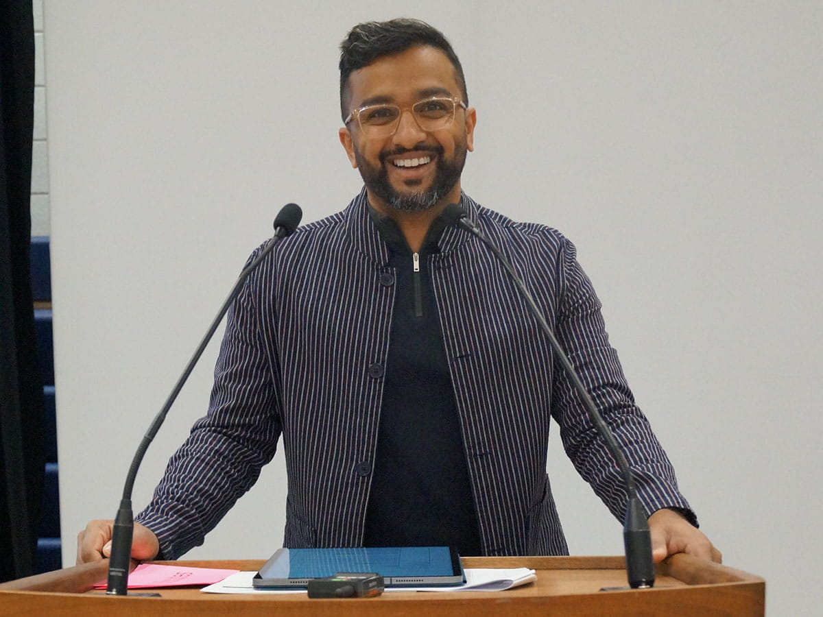 Sheldon Pereira standing behind a podium and smiling.