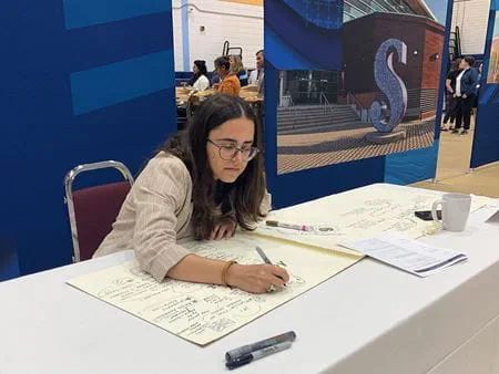Sheridan alumna Nazrin Alaskarov seated at a table drawing in front of a Sheridan back drop.