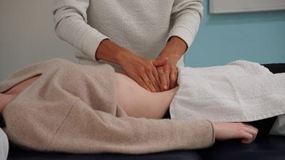 Student treating the stomach of a student lying on an examination table at Sheridan's Osteopathy Care Clinic.