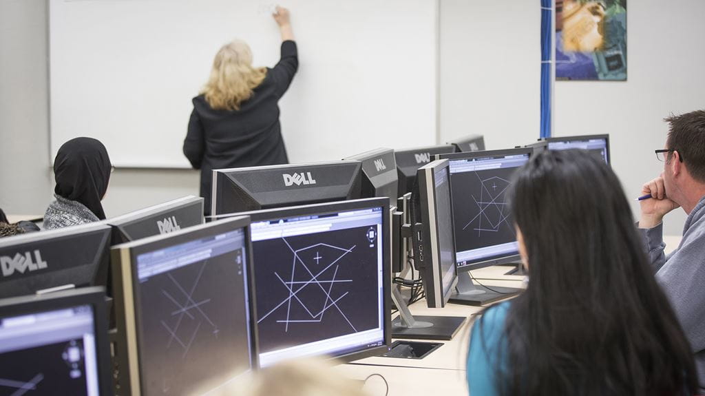 Students with computers in a CAD lab watching a teacher write on a white board