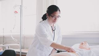 A student nurse using her stethoscope to examine a patient-care mannequin in a bed