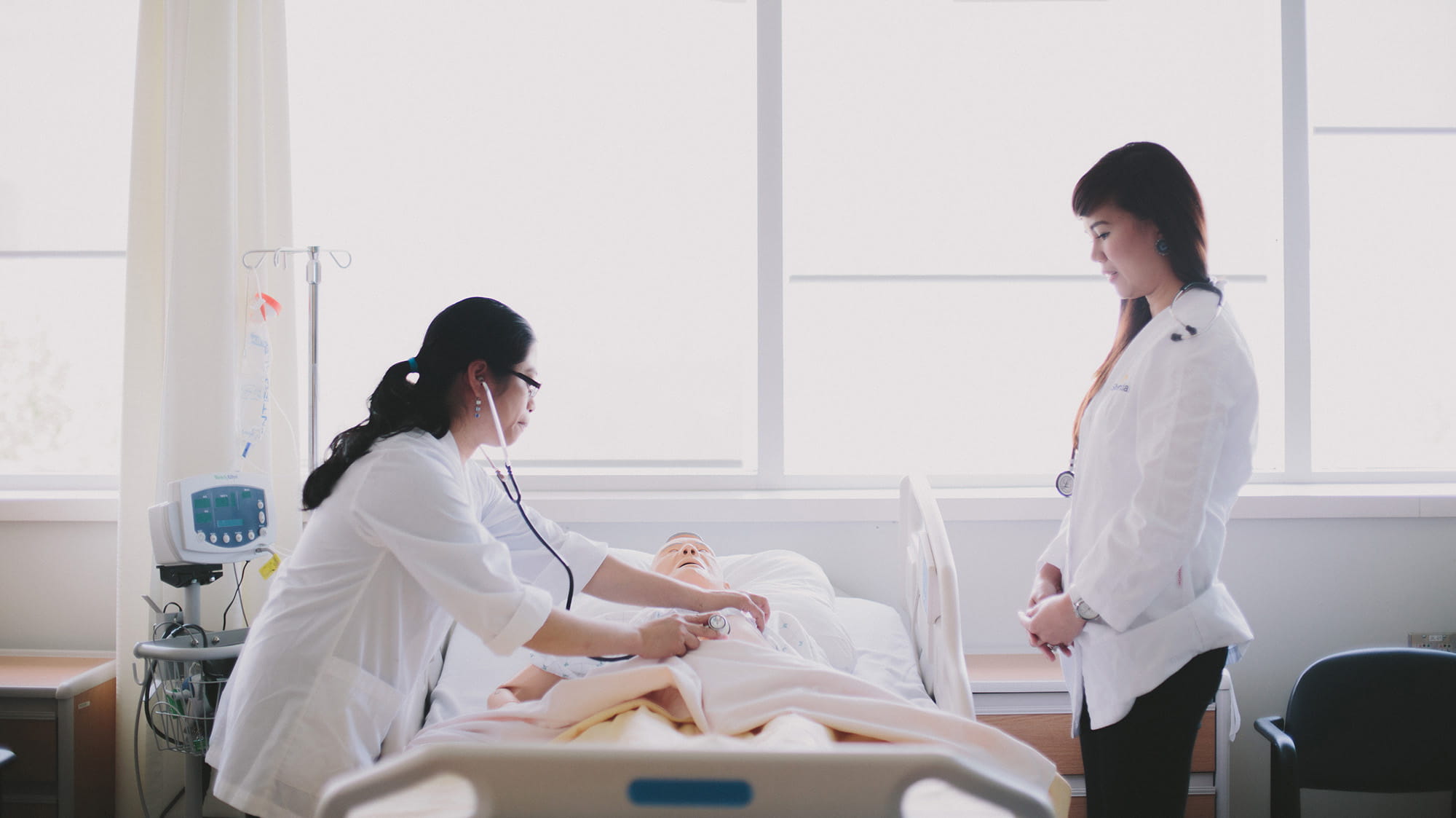 Two nursing students examining a patient mannequin in a bed