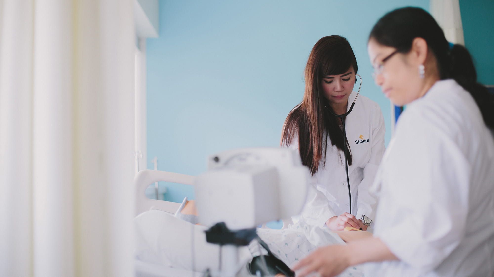 Two student nurses examining a patient in a bed