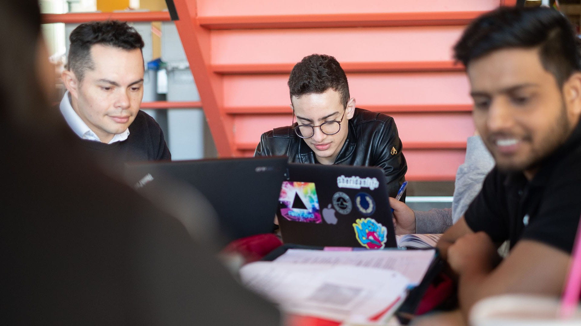 Three students studying together at a table with laptops