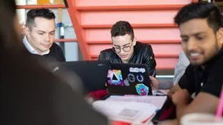 Three students studying together at a table with laptops