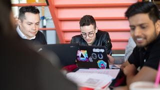 Three students studying together at a table with laptops