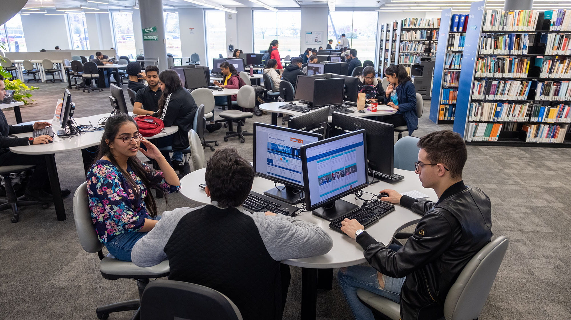 Students at tables near rows of books at the library