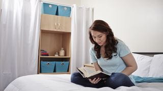 A girl reading a book on her bed in her residence room