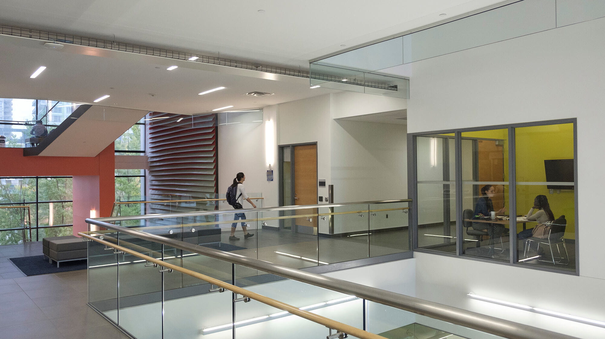 A hallway with stairs and a view inside a glass-walled Group Study Room