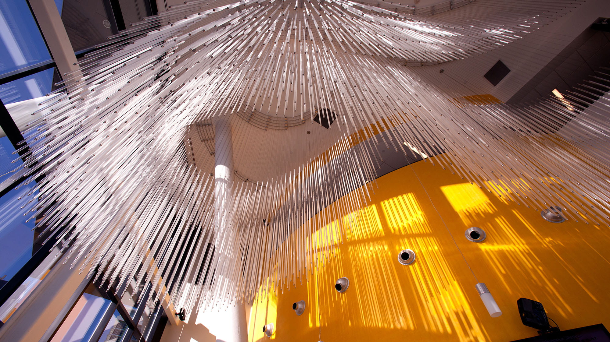 The view looking up at a sculpture of long strands of glass hanging from the ceiling
