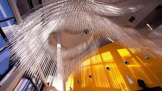 The view looking up at a sculpture of long strands of glass hanging from the ceiling