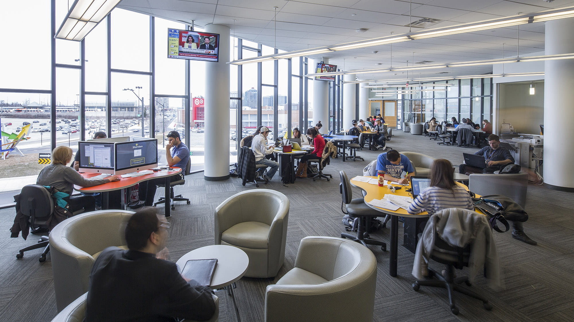 Students working at tables in a large library with lots of windows