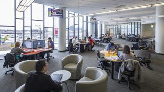 Students working at tables in a large library with lots of windows