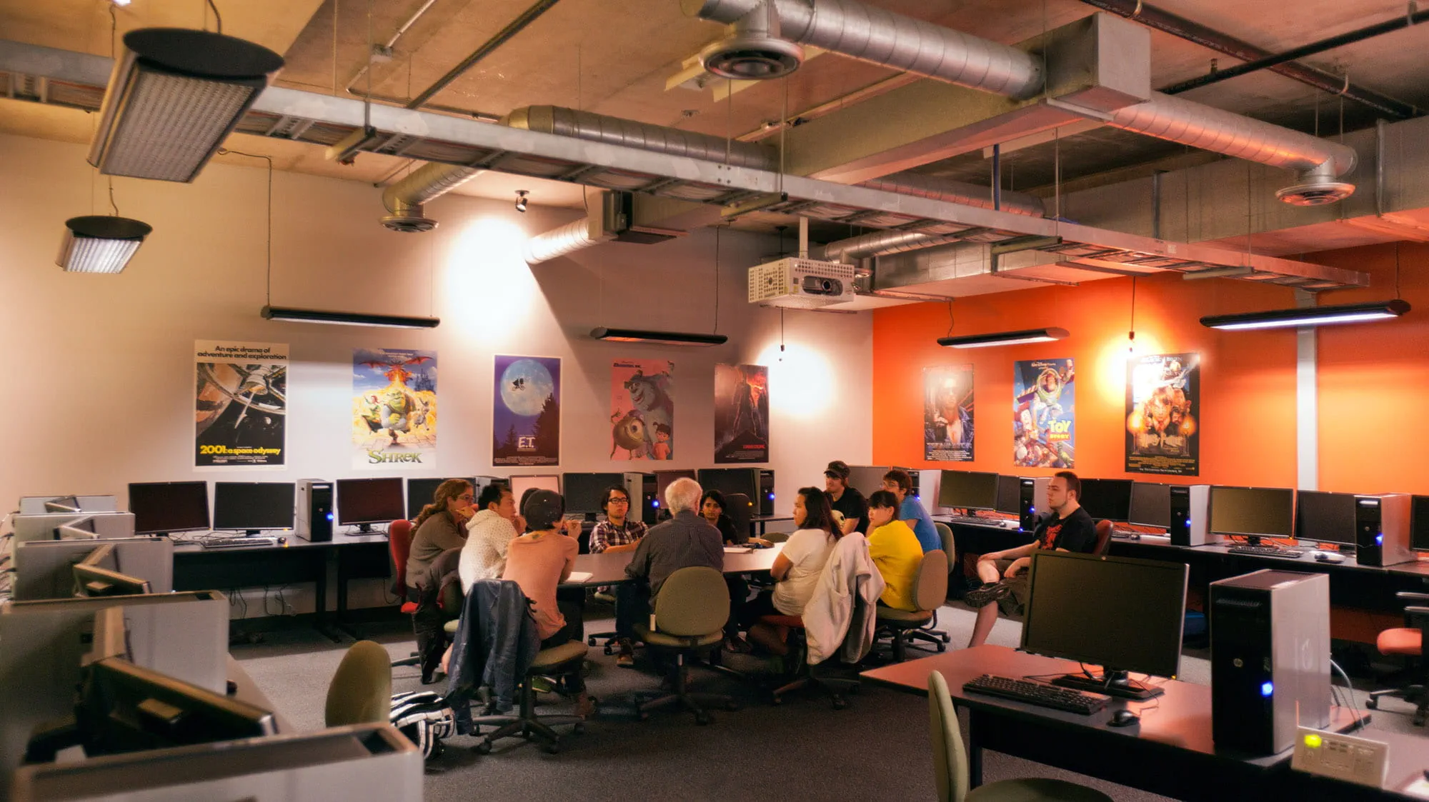 An instructor talking to a group of students in a room with lots of computers and posters of animated films on the walls