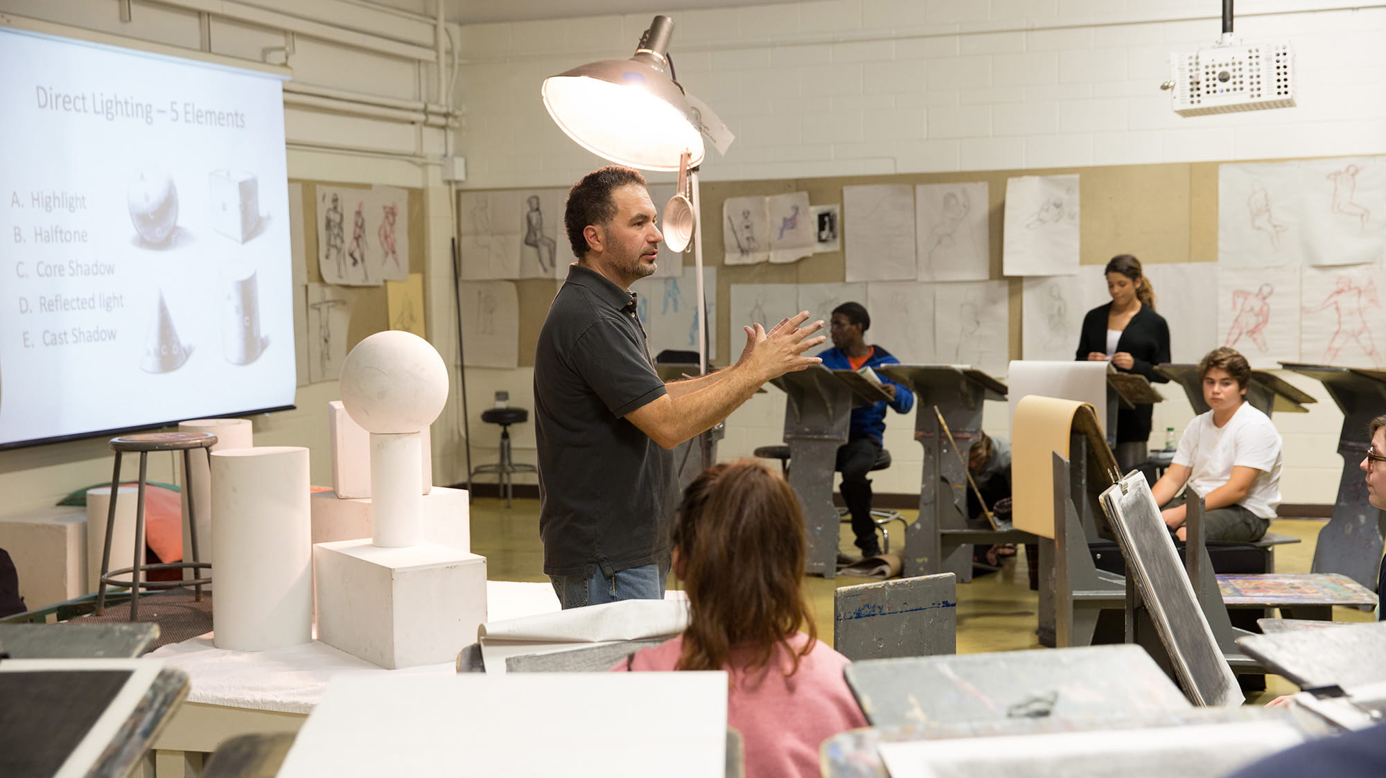 An instructor talking to a class full of students working on easels
