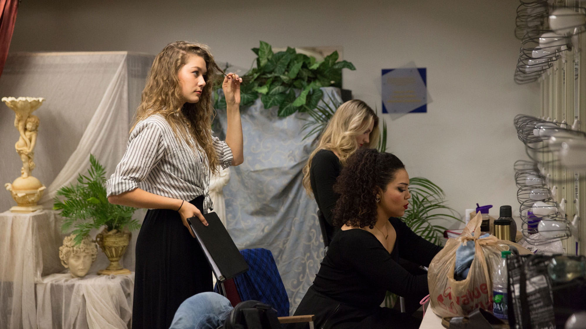 Three female Musical Theatre students doing their hair and makeup before a show.