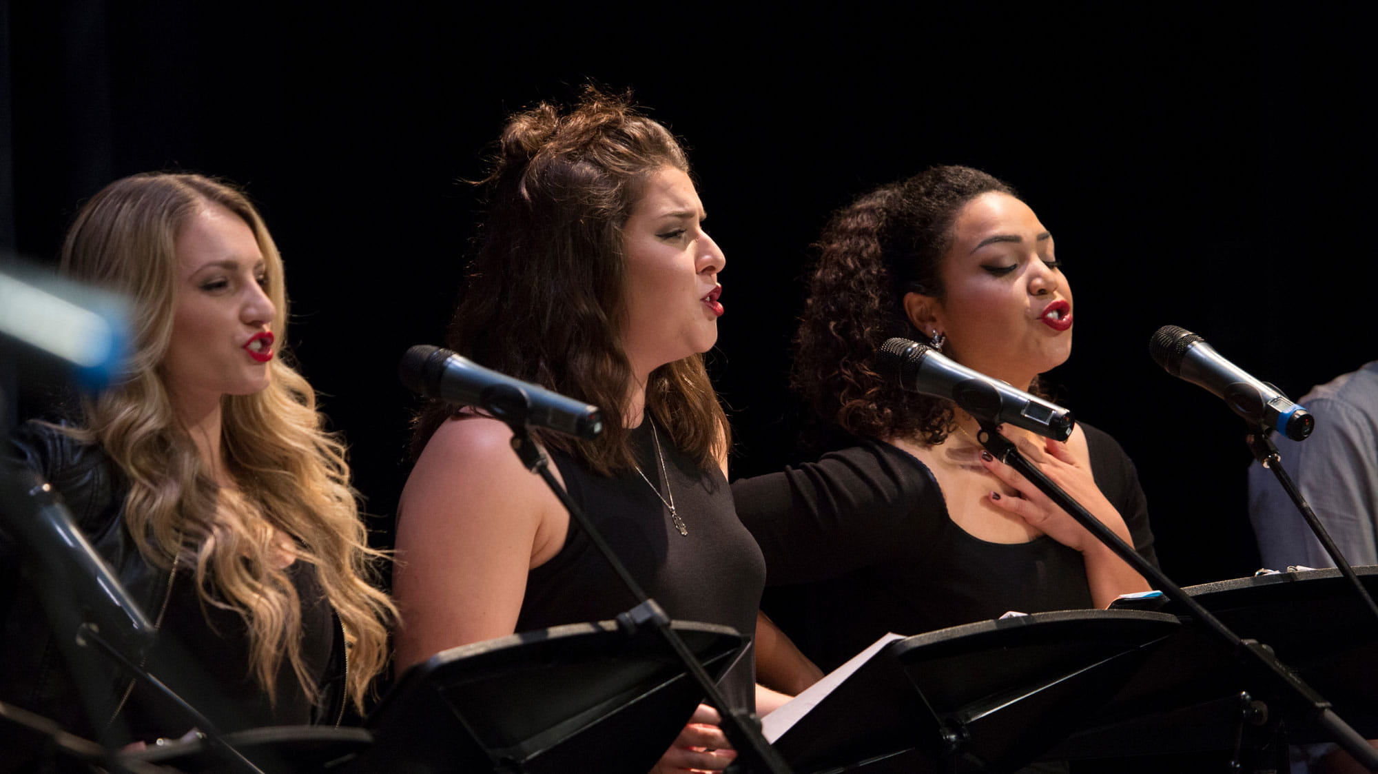 Three female Musical Theatre students singing into microphones.