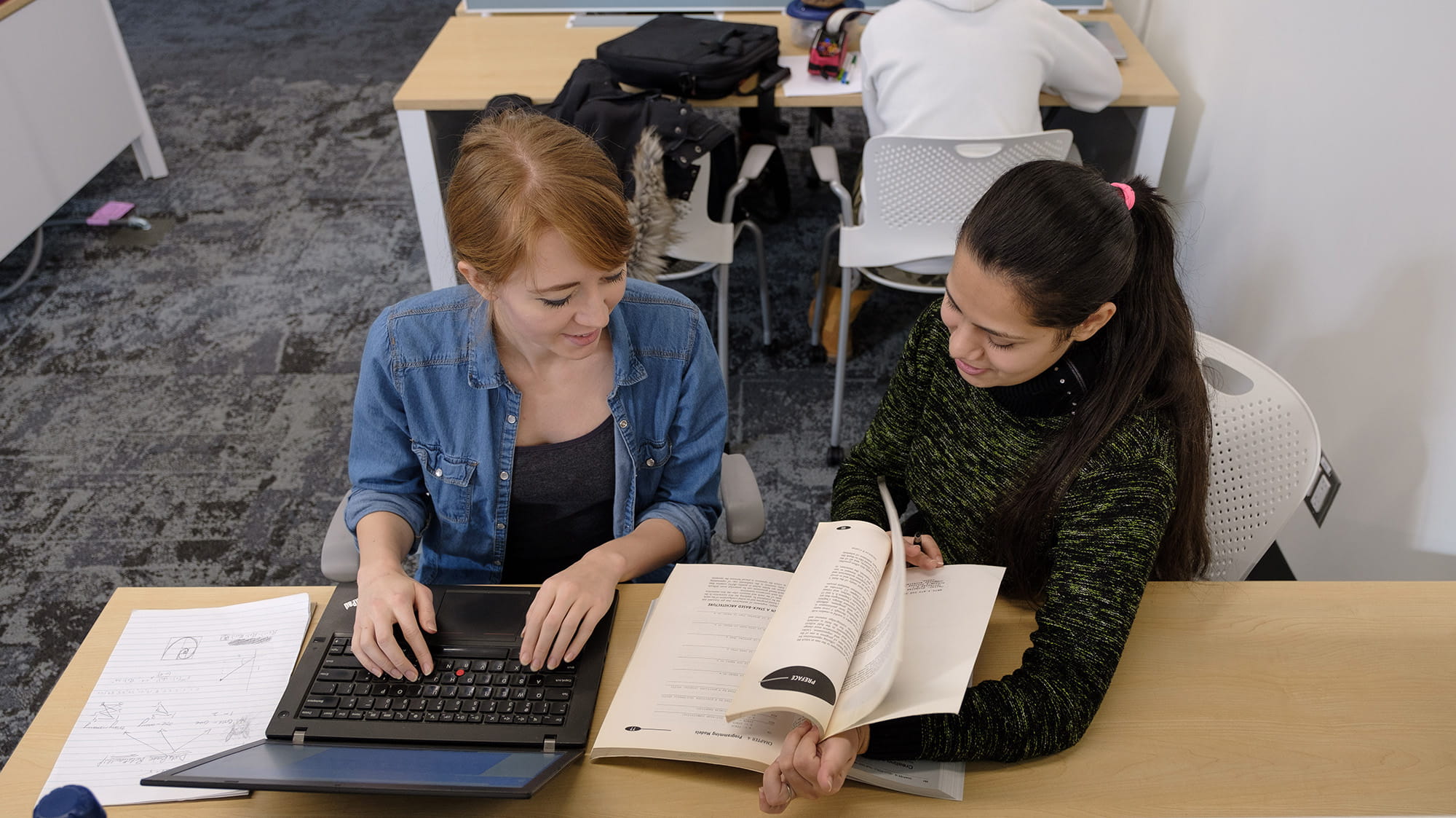 Two students working together on a project at a desk in the library
