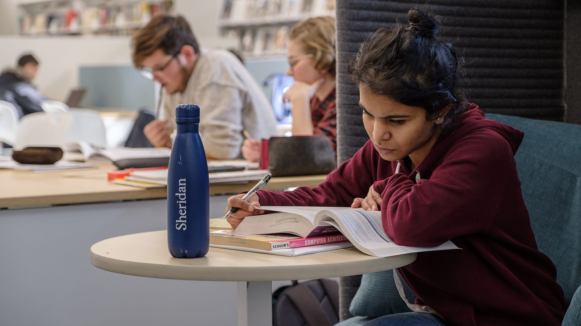 A student reading a textbook while sitting at a table in the library