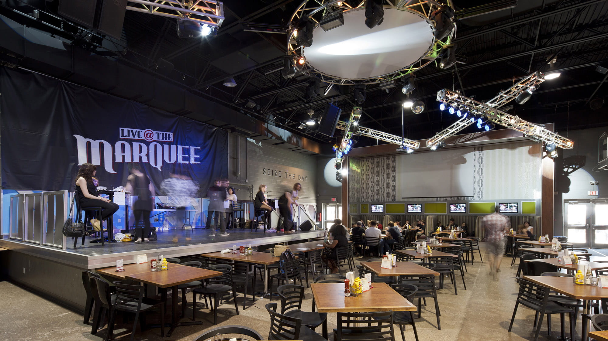 A dark room with tables, a stage, and a purple lit Marquee sign