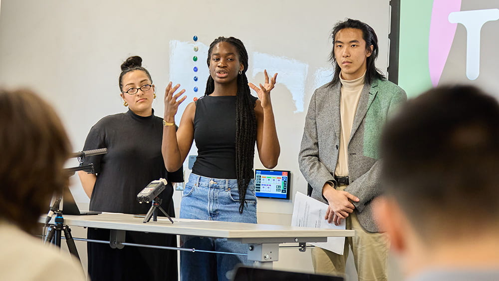 Three people standing at the front of a room addressing an audience