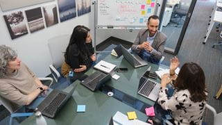 Four people seated around a table with laptops in front of them