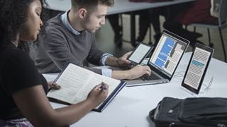 Students working with a laptop, tablets and writing on paper