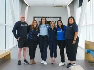 Six people standing side-by-side in a hallway, posing for a photo