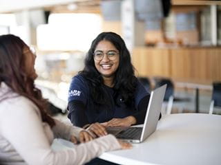 Students smiling with a laptop on the table in front of them
