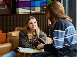 Students talking with a notebook open on a table between them