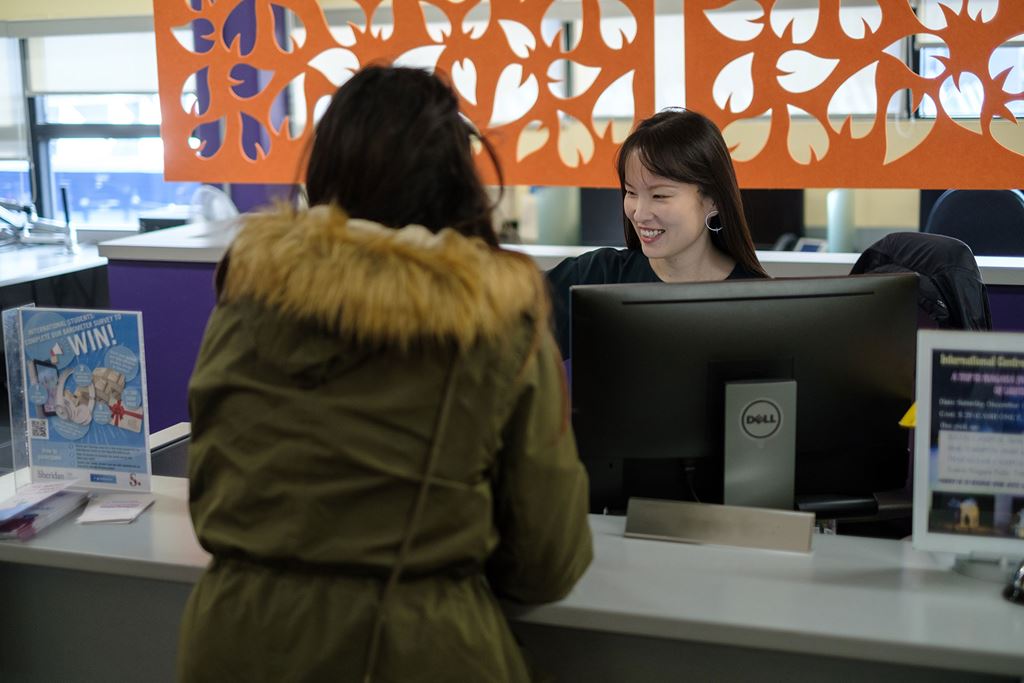 A person standing at a service desk speaking with an employee.