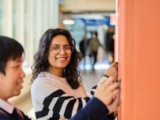 Two students smiling in a hallway as they open lockers
