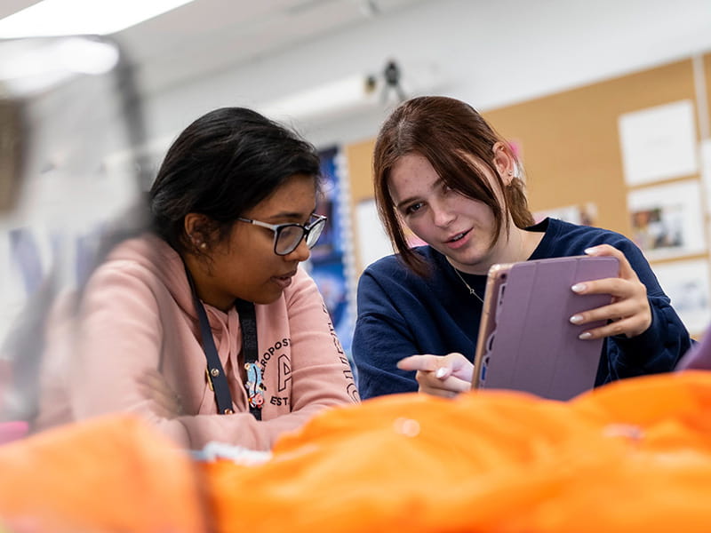 Two students working together in front of a tablet.