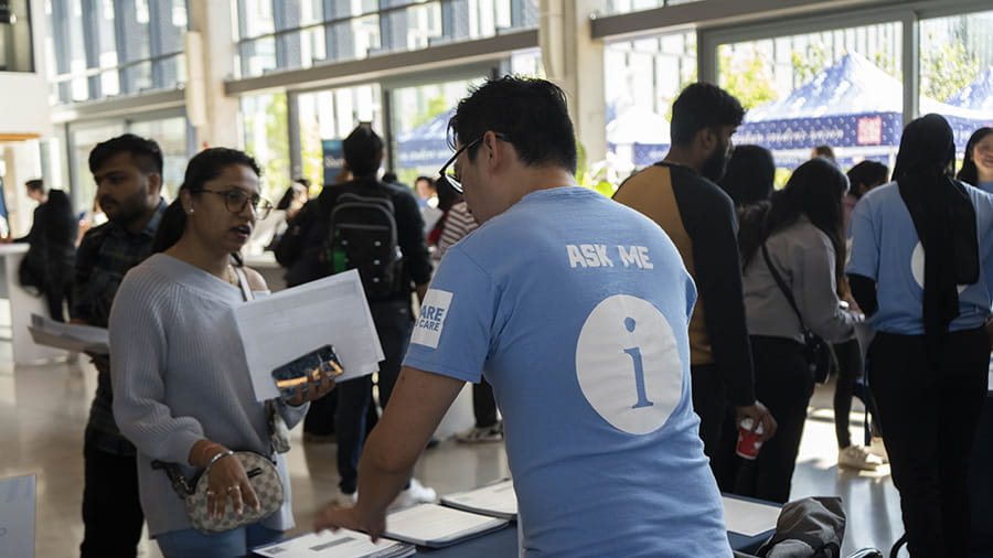 A person talking to a Sheridan representative who is wearing an 'Ask Me' t-shirt