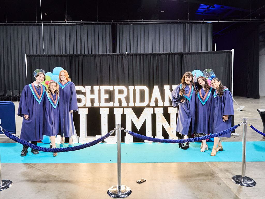 Graduates posing in front of the 'SHERIDAN ALUMNI' marquee at Convocation