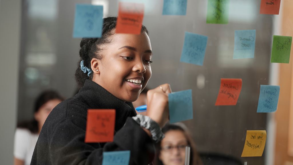 Student writing on a sticky note that is stuck to a piece of glass