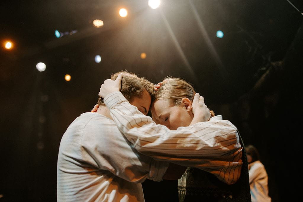 Students in costume embrace while performing on stage