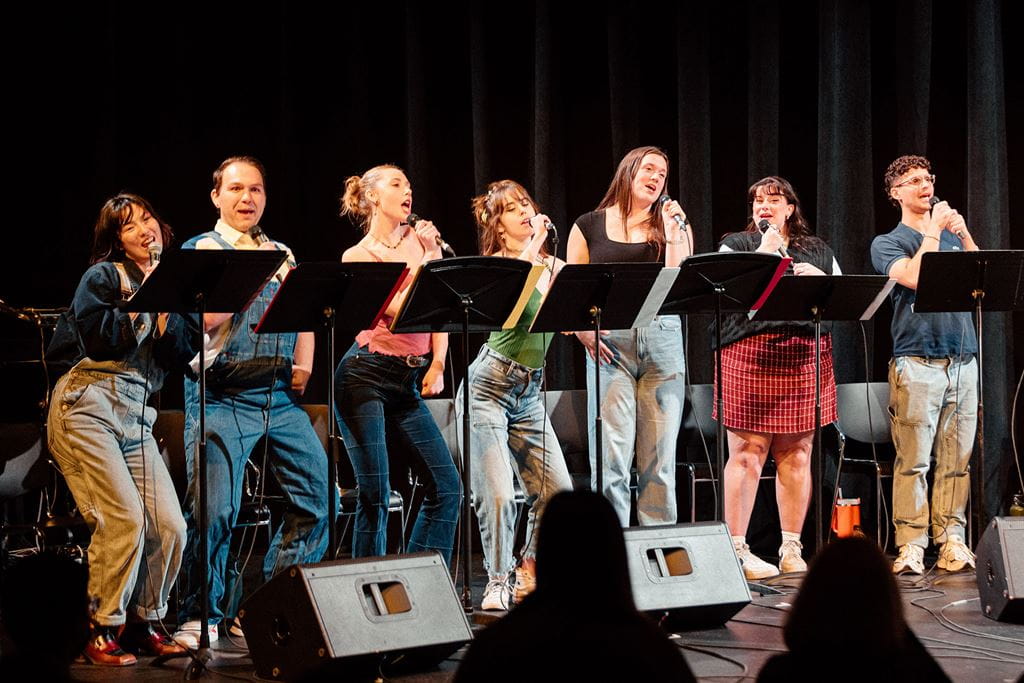 Group of students holding microphones and singing while standing behind music stands