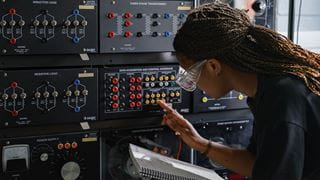 Person examining an electrical board while holding a notebook