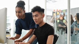 Two students working together in front of a large computer screen.