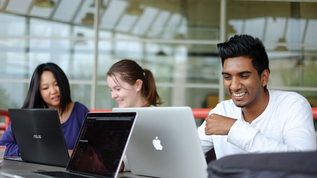 Students smiling while seated behind laptop screens