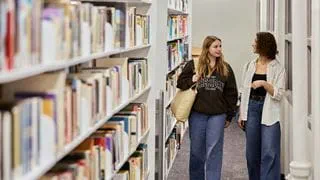 Two students walking and talking in the library.