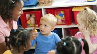 An adult sitting on the floor with a group of children in a childcare setting