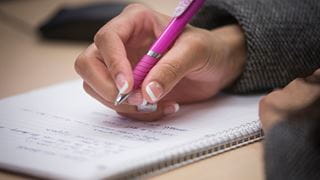 Hand holding a pen and writing in a notebook