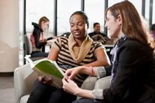 Two people sitting in wing chairs looking at a book together