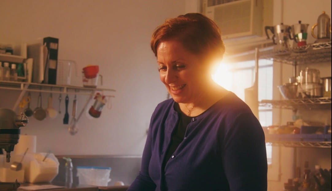 A woman, Anna Sottile, is photographed smiling in her kitchen with the light streaming in behind her.