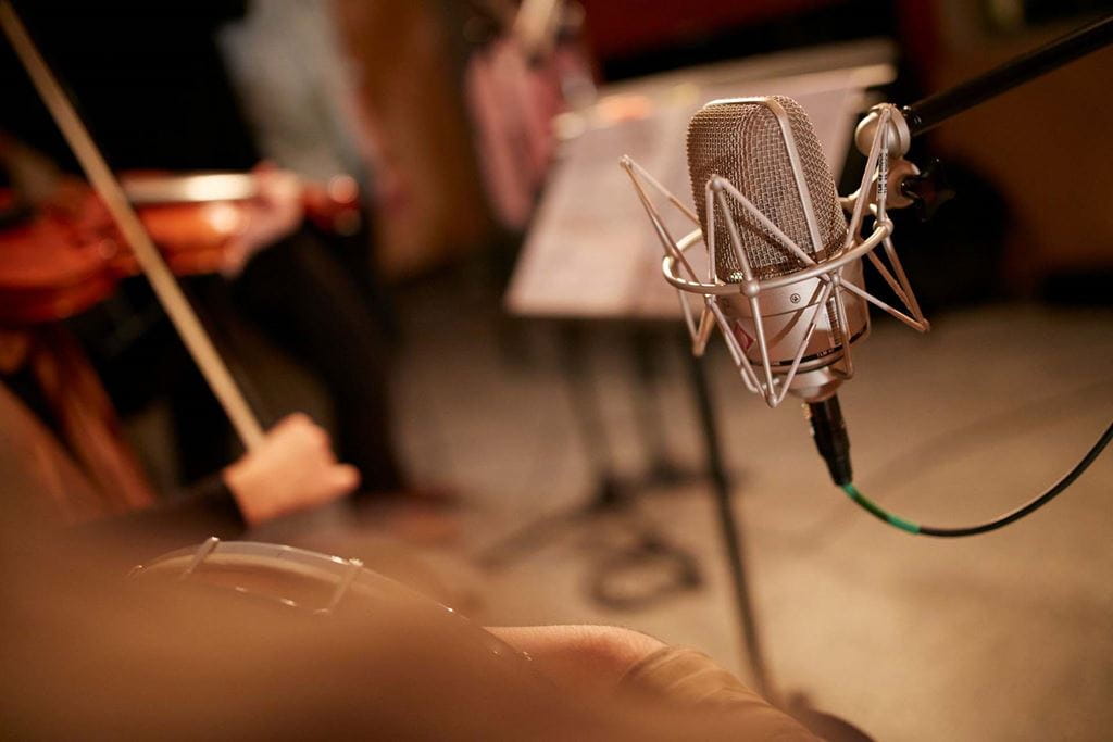 Close-up of a microphone. A violin can be seen being played in the background.
