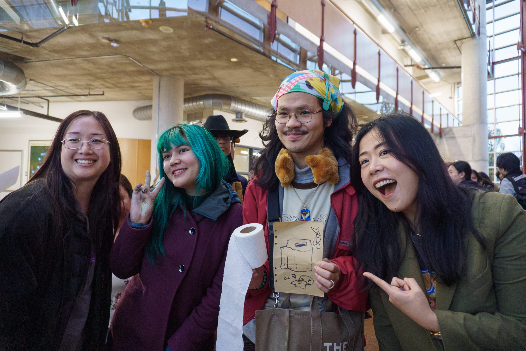 Three animation students pose for a photo with Domee Shi, with one student holding a roll of toilet paper in one hand and a drawing of a toilet paper roll as a nod to Shi's short film Bao