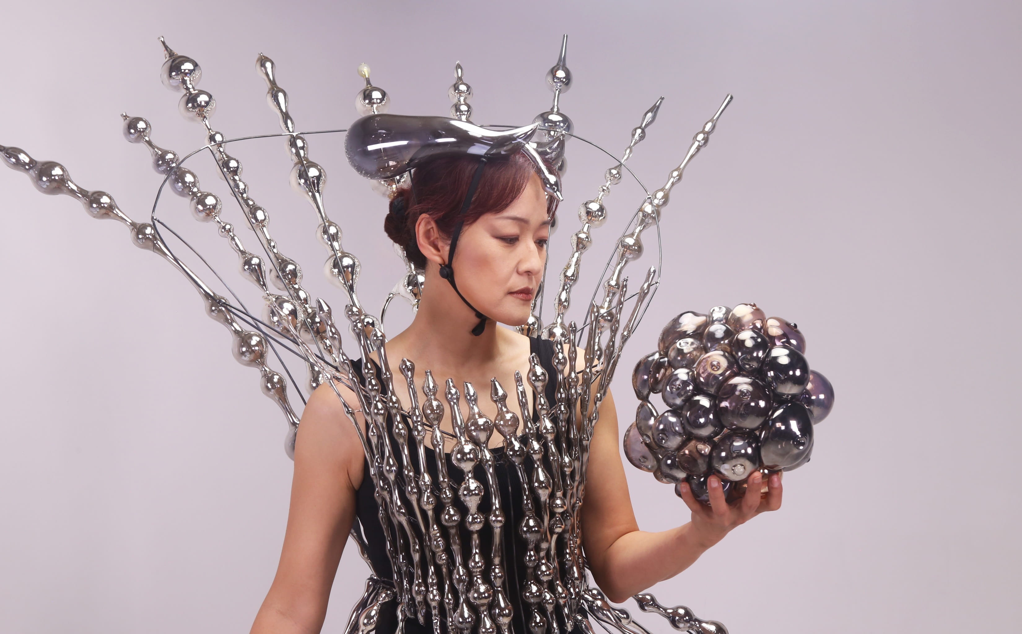 Instructor Jin Won Han wears an outfit made of glass while holding a glass ball.