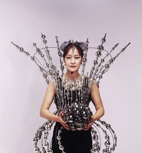 Instructor Jin Won Han wears an outfit made of glass while holding a glass ball.